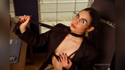 Elegant woman in a black blazer and glasses posing confidently in a modern office setting.
