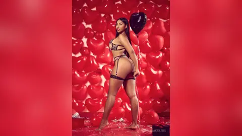 DayanaKeilers poses naked from the waist up, wearing black lace lingerie and a garter, against a wall of red heart-shaped balloons.
