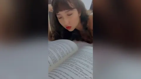Young woman with dark hair reading a book in a cozy, relaxed indoor setting.