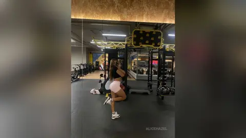 Athletic woman in black crop top and pink shorts posing in a modern gym mirror.