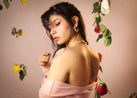 Elegant woman in a pink off-the-shoulder dress posing amidst rose petals for a romantic portrait.
