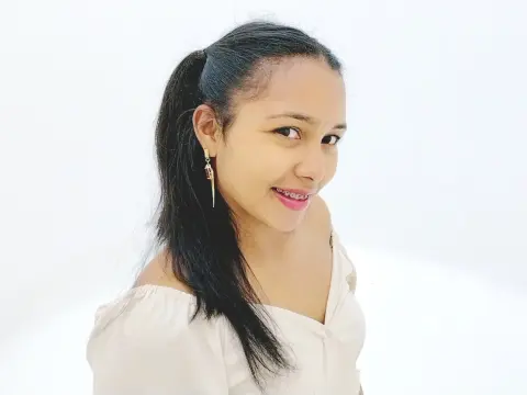 Ehmha smiles with her dark hair pulled back in a ponytail, wearing a white off-the-shoulder top against a plain white background.