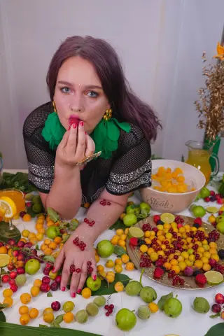 Woman in black mesh top with green accents posing amidst a vibrant spread of citrus fruits and berries.