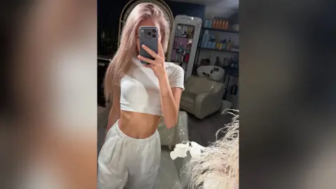 MarryDavies takes a mirror selfie wearing a white cropped t-shirt and matching white lounge pants, showing her flat stomach.