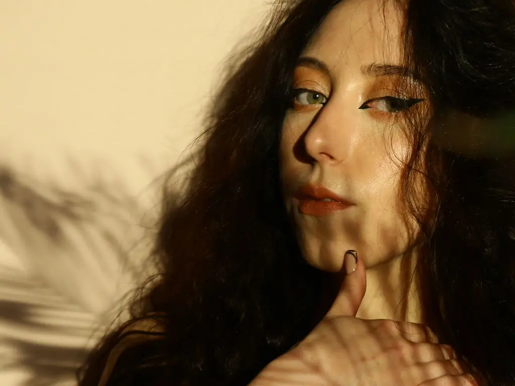 Close-up portrait of a woman with wavy dark hair and winged eyeliner in warm, cinematic sunlight.