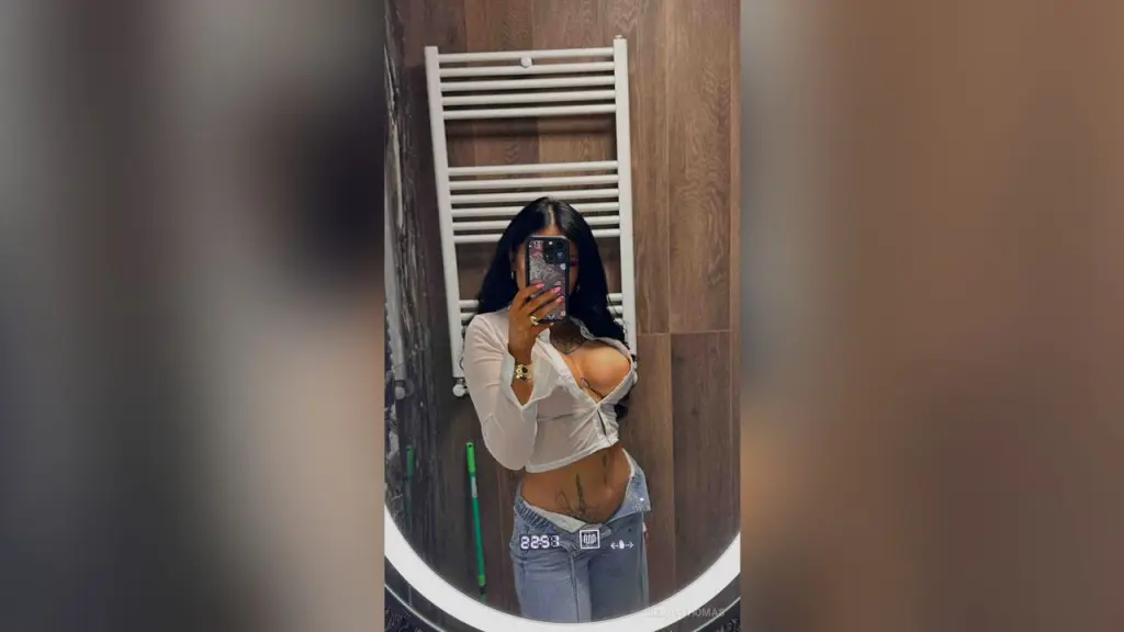 SiennaThomas β Young woman in a white crop top and denim jeans taking a mirror selfie in a modern bathroom.