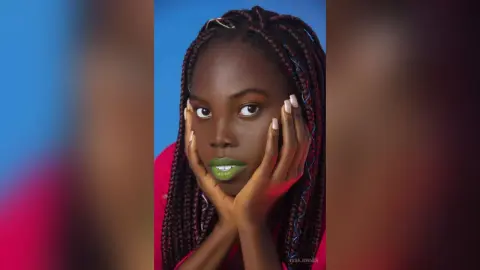 Beautiful Black woman with long braids and green lipstick posing against a blue background.