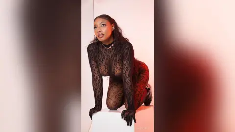 Elegant woman in a black lace bodysuit posing against a white studio background with a moody aesthetic.