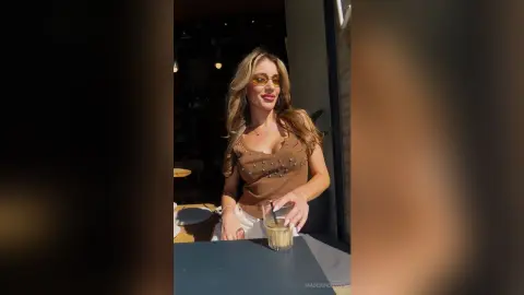 Stylish woman in a brown ribbed tank top and sunglasses enjoying a drink at an outdoor cafe.