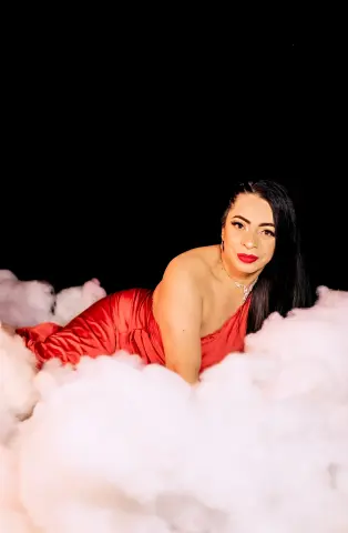 Elegant woman in a red satin dress reclining in soft white clouds against a black background.