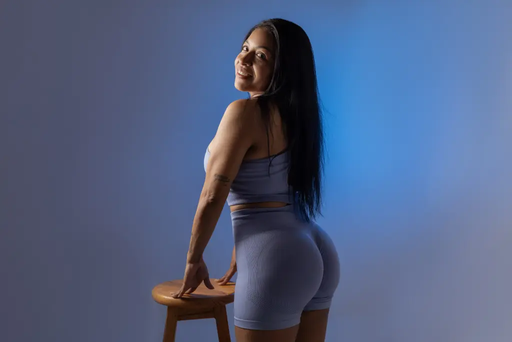 KiaraStonne smiles while posing sideways, wearing a pink crop top and denim shorts that show off her legs and waist.