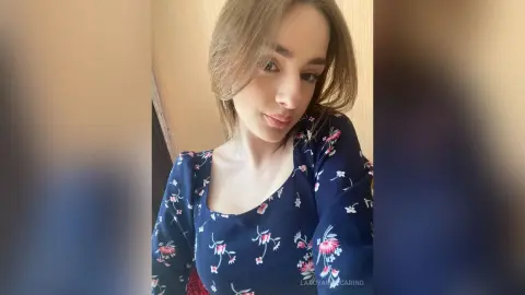 Young woman in a navy blue floral print blouse smiling in a warm indoor setting.