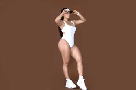 Athletic woman in a white one-piece swimsuit and sneakers posing confidently against a brown studio background.