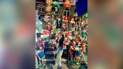 Woman in a plaid jacket standing amidst giant festive nutcracker decorations at a magical night Christmas display.