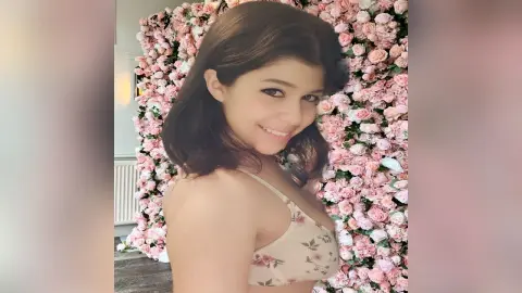 Smiling young woman in a floral print bikini top posing in front of a romantic pink rose wall.