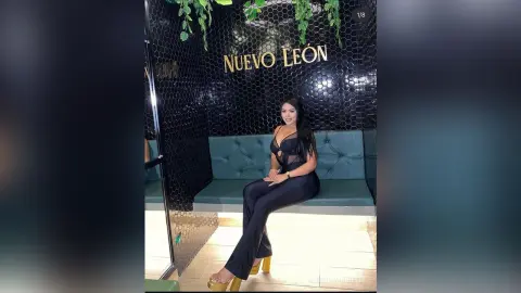 Smiling woman in a black jumpsuit sitting on a teal velvet sofa in a modern Nuevo Leon lounge.