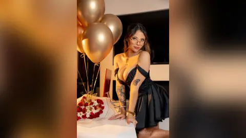 RebecaVillalobos wears a black off-the-shoulder dress while posing next to gold balloons and red roses.