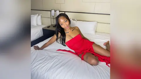 Smiling Black woman in a red dress relaxing on a white bed in a bright hotel room.