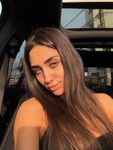 Young woman with long brown hair smiling in a car during golden hour sunset light.