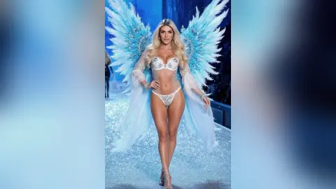 JessycaPage poses in a sparkly blue angel costume with large feathered wings and sheer white lingerie.