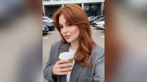 Redheaded woman in a grey blazer holding a coffee cup in an urban parking lot setting.