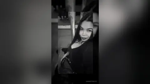 Smiling young woman in a black outfit posing for a moody black and white portrait outdoors at night.