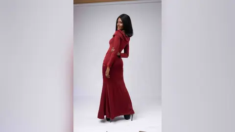 Elegant woman in a long red evening gown posing confidently in a bright studio setting.