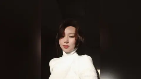 Young woman in a white turtleneck sweater looking serene in soft, warm sunlight.