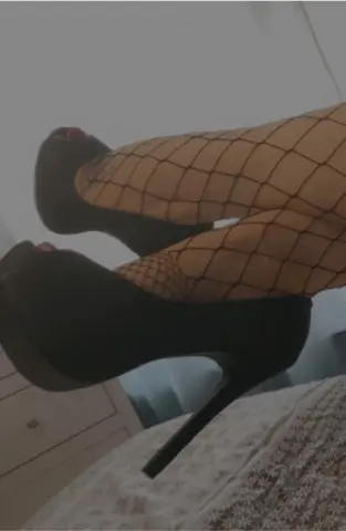Close-up of legs in black fishnet stockings and high platform stiletto heels on a bed.