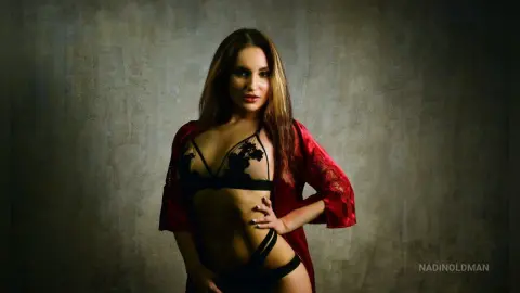 Beautiful woman in black lace lingerie and a red silk robe posing against a textured dark background.