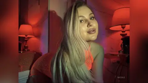 Blonde woman in an orange mesh top posing in warm red lighting for a moody indoor portrait.