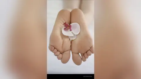 Close-up of bare feet holding a delicate pink orchid flower in a serene, minimalist setting.