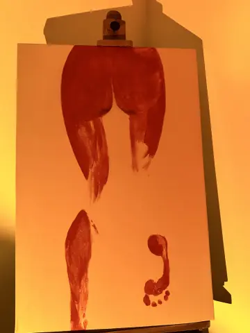 Abstract red paint silhouette of a human body on a white canvas easel under warm orange lighting.