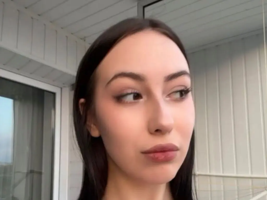 Young woman with long dark hair and natural makeup looking away in a bright modern room.