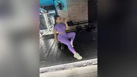 Athletic woman in purple gym set taking a mirror selfie in a moody industrial fitness studio.