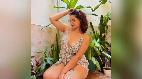 Smiling woman in a floral summer romper posing in a bright indoor garden setting.