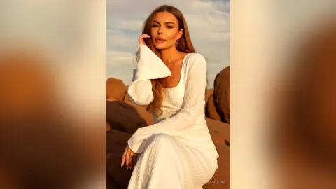 Elegant woman in a white long-sleeve dress posing in a desert landscape during a golden sunset.