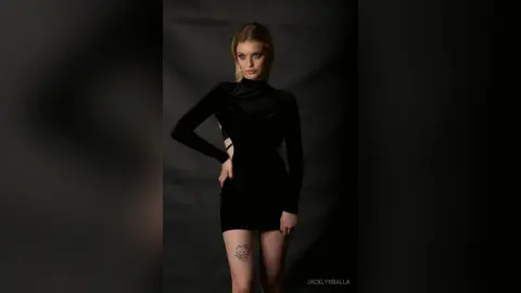 Elegant woman in a chic black long-sleeve mini dress posing against a dark moody studio background.