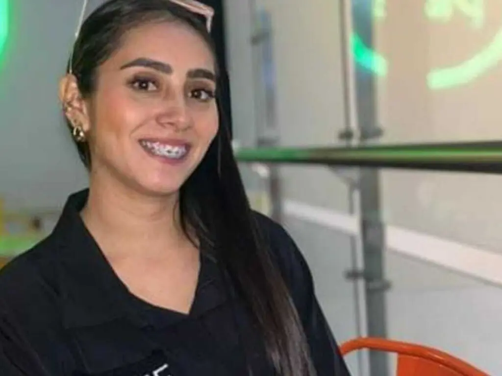 Smiling young woman with long dark hair wearing a black shirt in a bright indoor setting.