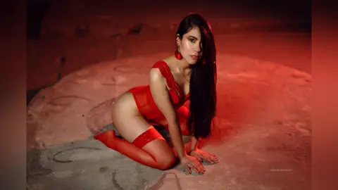 SamanthaHarvey kneels on a stone floor wearing red lace lingerie and red thigh-high stockings.