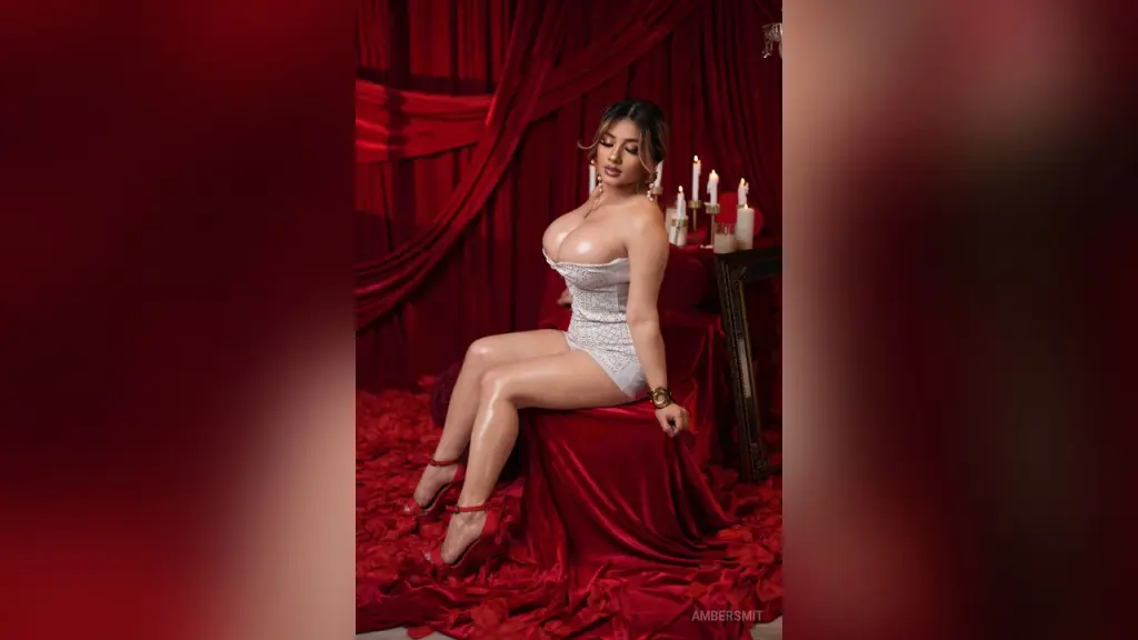 AmberSmit — AmberSmit sits on a red velvet chair wearing a tight, sparkly silver bodysuit against red curtains.