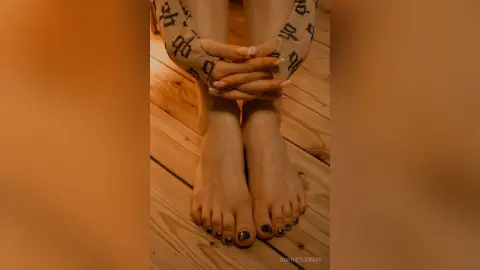 Close-up of a person's bare feet and patterned leggings resting on a rustic wooden floor in warm lighting.