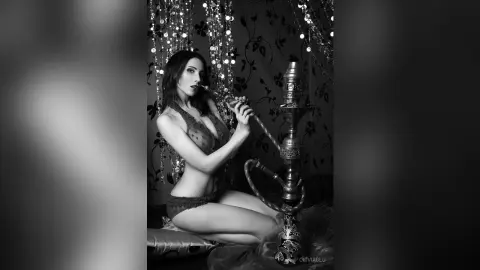Glamorous woman in lace lingerie sitting by a hookah in a moody, dark aesthetic black and white setting.