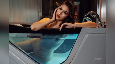 Relaxed young woman with wavy hair relaxing in a modern bathtub filled with clear blue water.