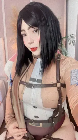 Cosplayer in Mikasa Ackerman outfit from Attack on Titan posing in a soft indoor setting.