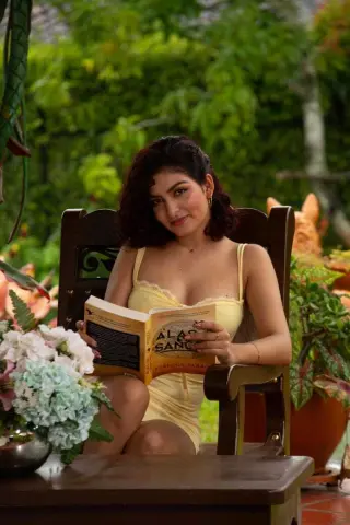 Young woman in a yellow sundress reading a book in a lush green garden setting.