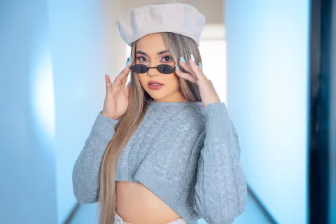 Stylish woman in a grey knit sweater and beret posing in a bright, minimalist hallway.