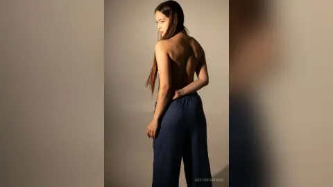 Elegant woman in navy blue wide-leg trousers posing with her back turned in a minimalist studio setting.
