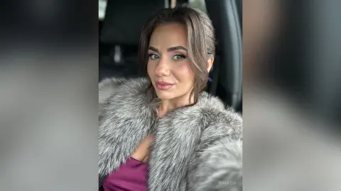 Smiling woman in a luxurious grey faux fur coat sitting inside a car for a glamorous portrait.