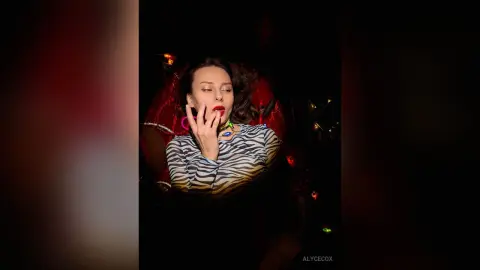 Elegant woman in a zebra print top posing with red lips in a moody, dark setting.
